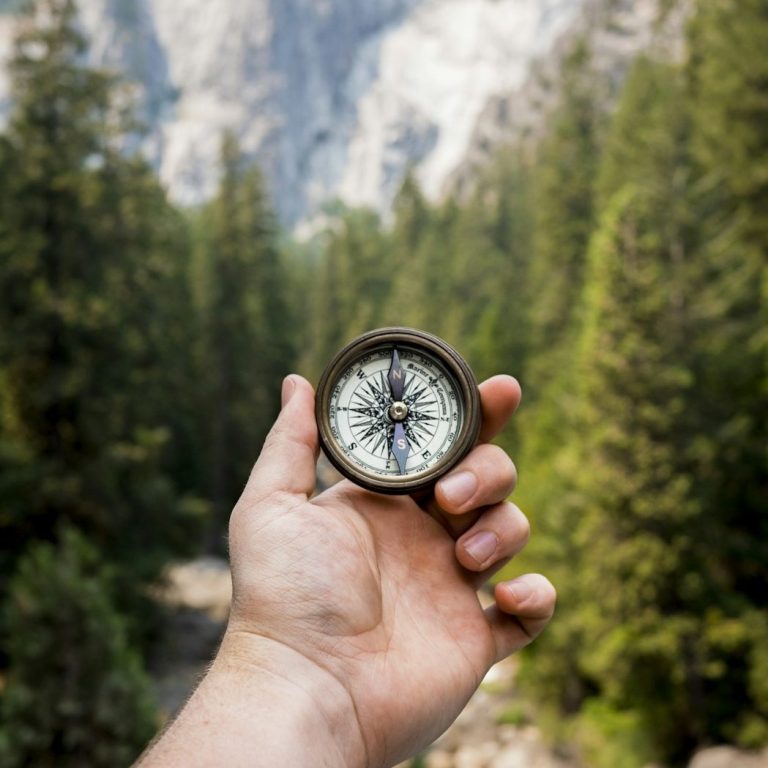 ZonoExplore GPS-Expedition Wandertag in NRW für Schulklassen mit Zonovo Eine Hand hält einen Kompass in der Natur, um sich auf einer GPS-Tour zu orientieren.