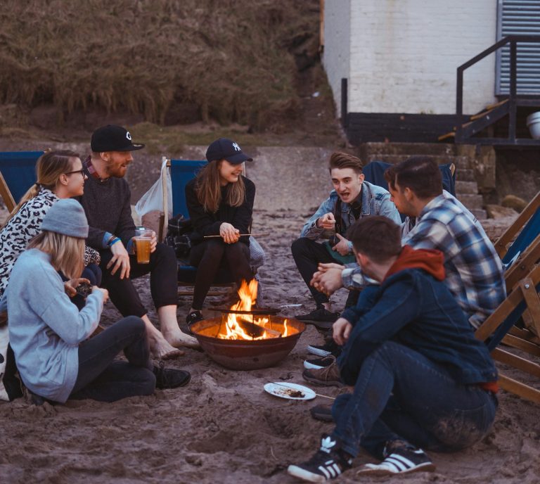 Jugendliche sitzen während ihrer Klassenfahrt an einer Feuerstelle und erzählen und lachen gemeinsam.